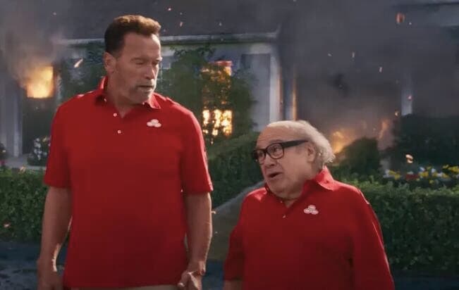 Super Bowl ad scene: two men in red polo shirts talk calmly in front of a burning house